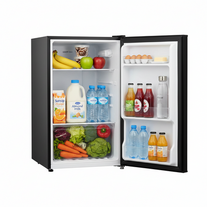 A compact single-door refrigerator shown open on a white background, stocked with food and beverages including bananas, apples, milk, juice, carrots, broccoli, and bottled drinks.
